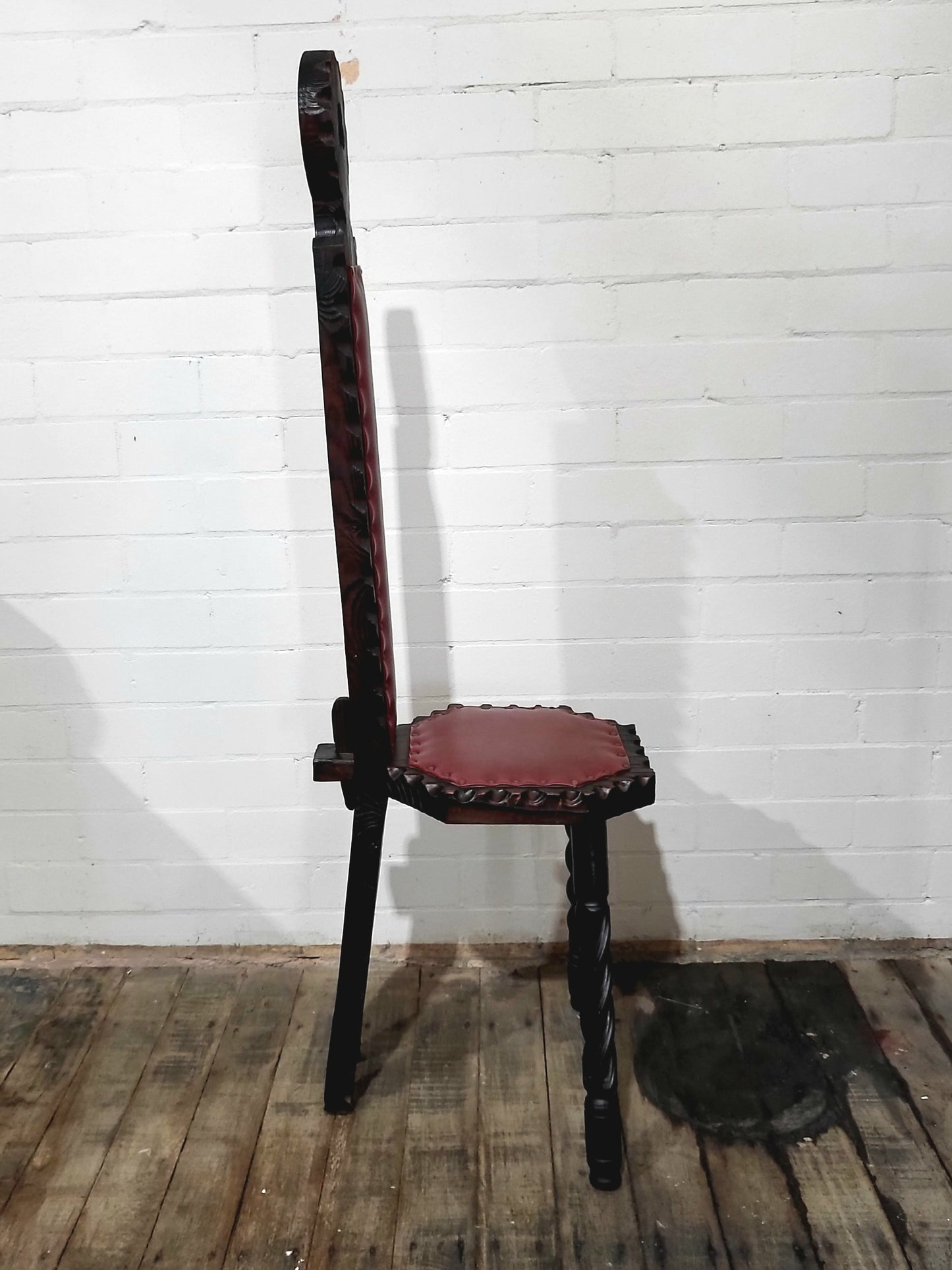 Side view of vintage Spanish Brutalist style chair with carved dark wood frame and oxblood red vinyl upholstery, Made in Spain