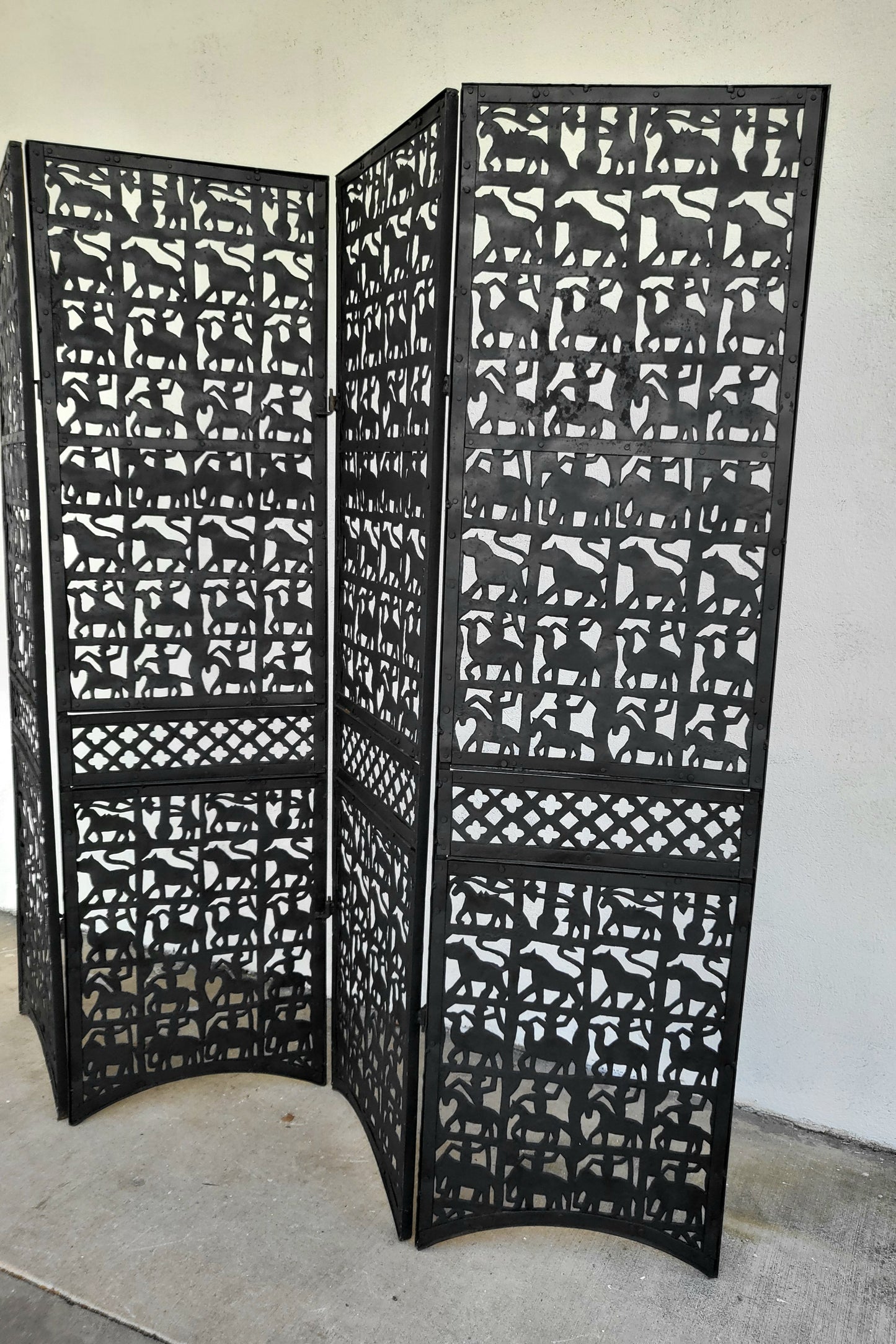 Angled side view of sculptural black metal screen, highlighting repeating rows of animals and decorative lattice band.