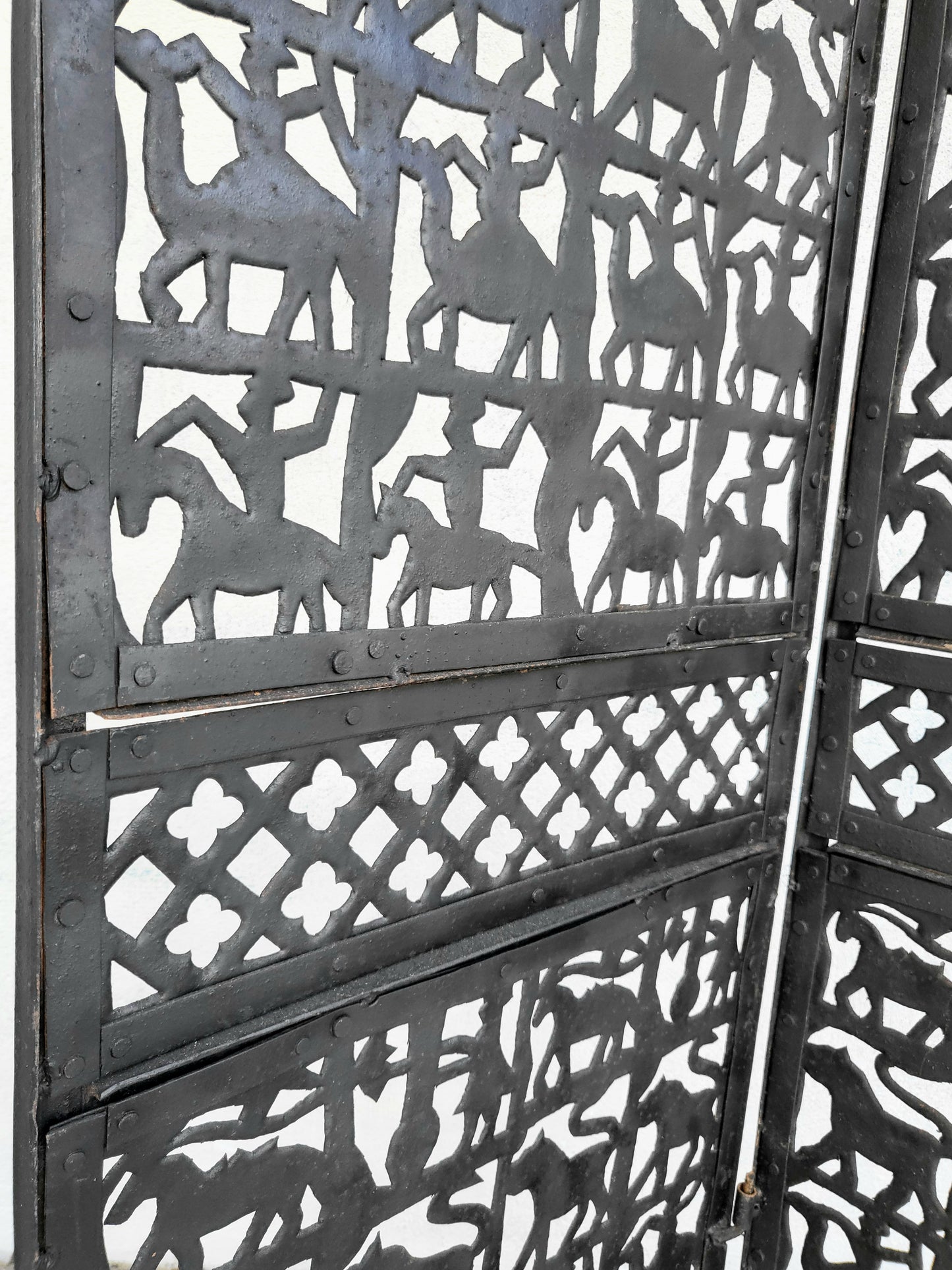 Close-up view of the wrought iron panel showing cut-out animal motif with textured surface and riveted joinery.