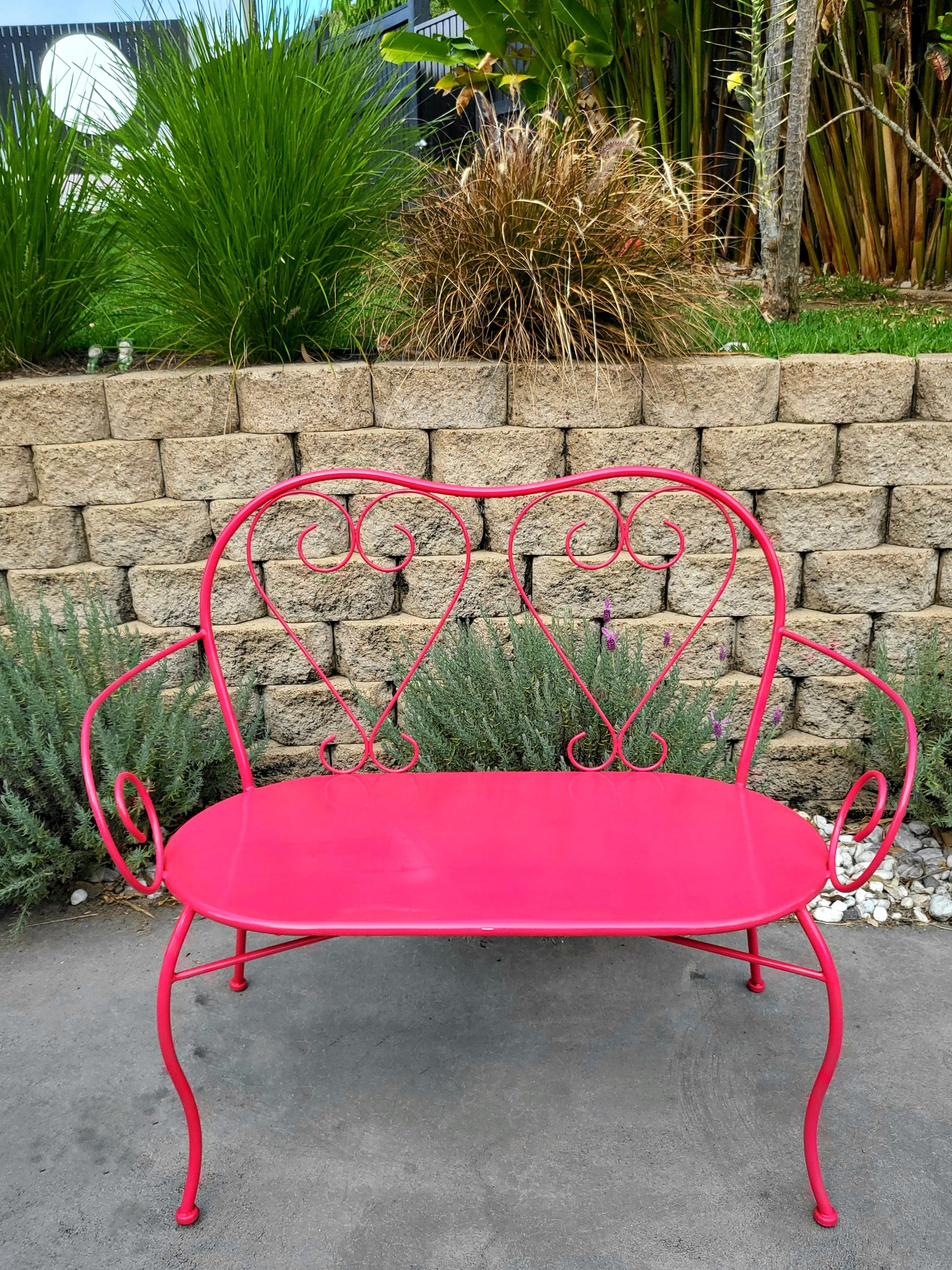 French mid-century metal love seat with heart-back design, powder-coated in vibrant pomegranate red, styled outdoors.
