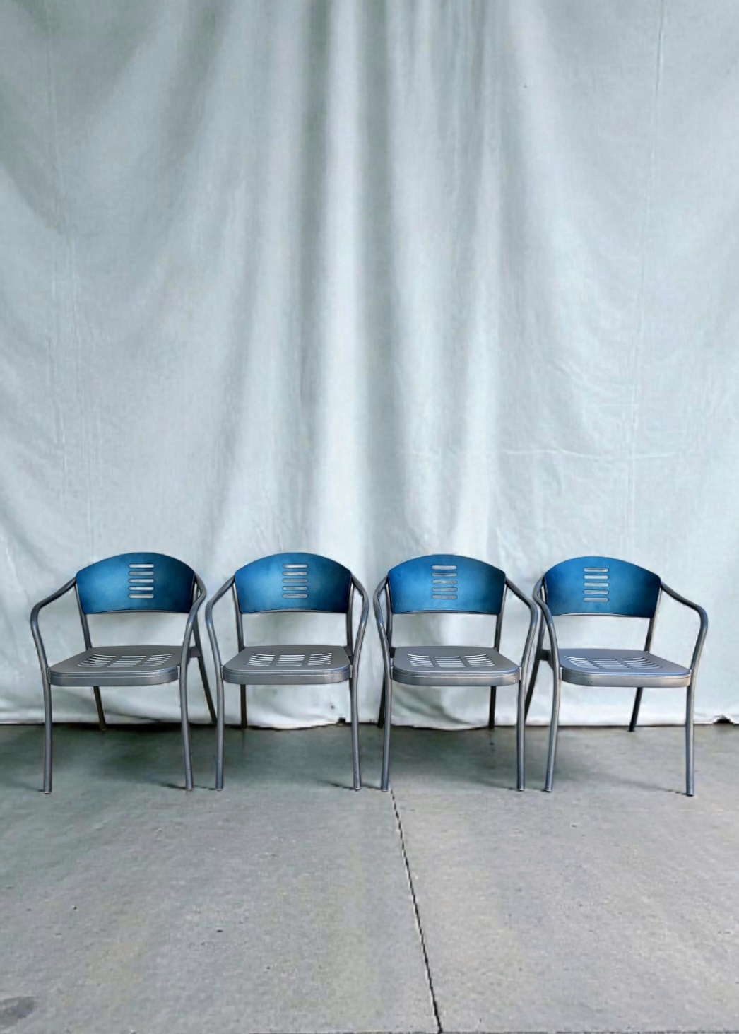 Four Vico Magistretti chairs lined up against a white curtain backdrop