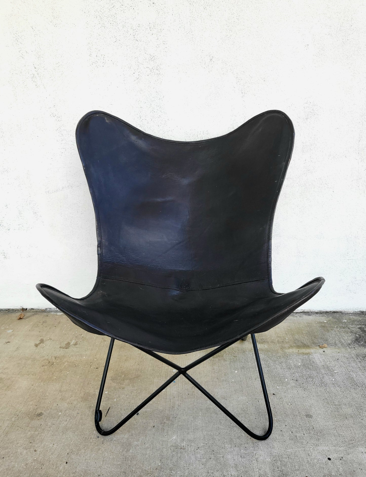 Black leather butterfly chair with sculptural metal frame, photographed against a white background.