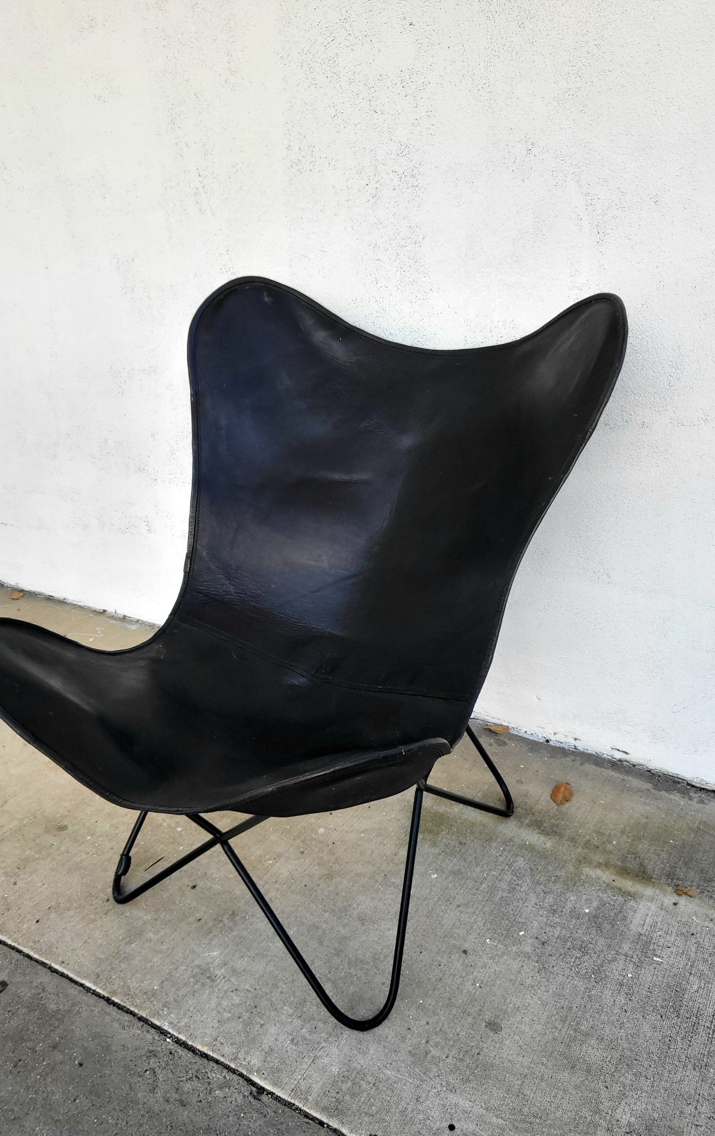 Butterfly chair with black leather sling and curved metal base, shown from an angled perspective.