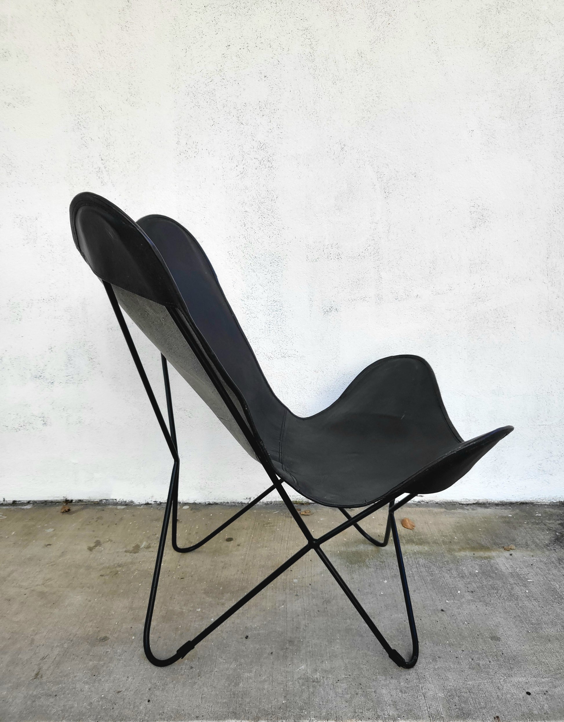 Profile view of a butterfly chair, highlighting the curved leather seat and slim metal legs.