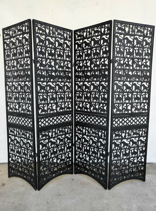 Four-panel black metal folding room divider with hand-cut animal silhouettes and lattice detailing, standing outdoors against a white wall.