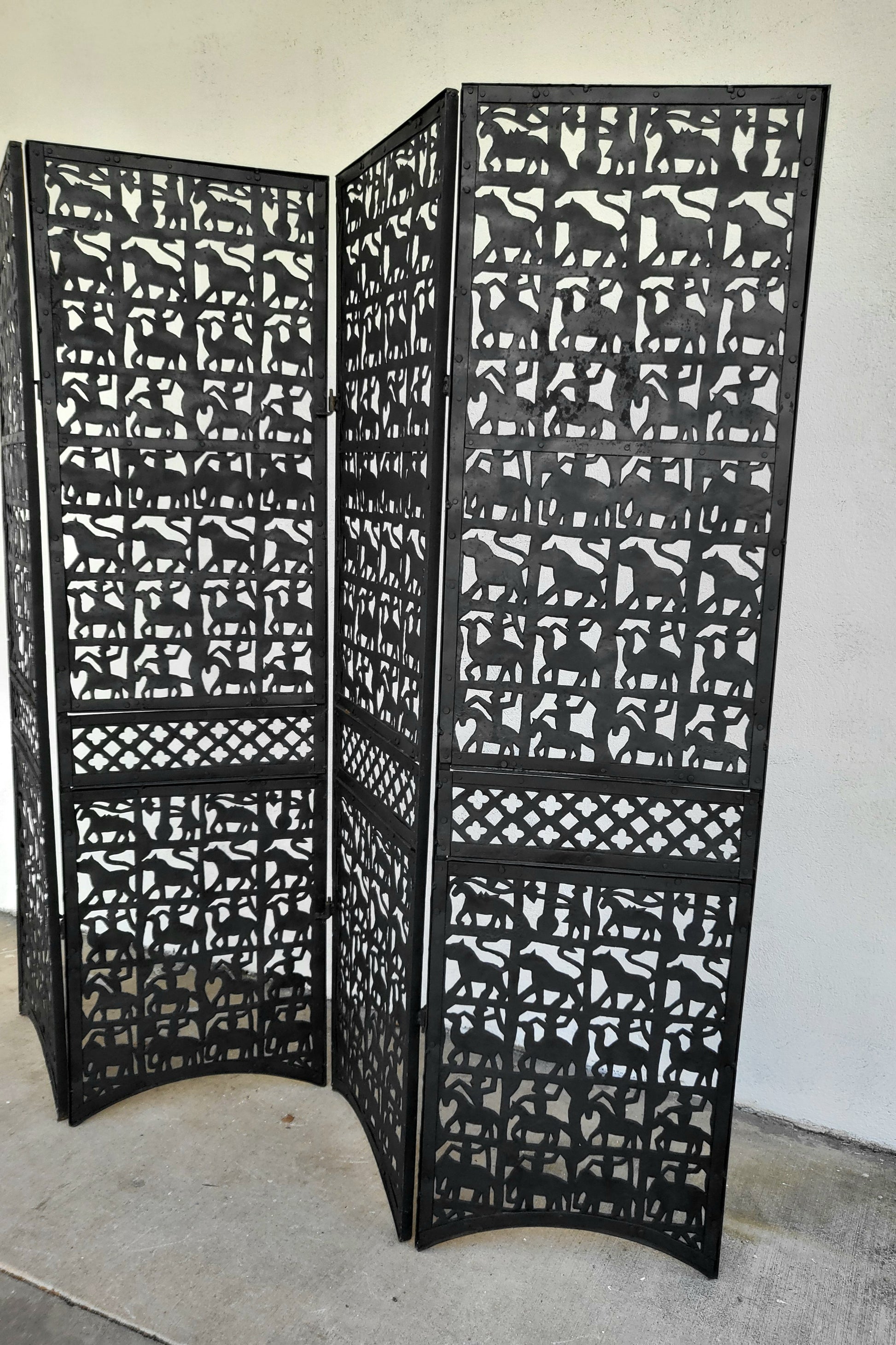 Angled side view of sculptural black metal screen, highlighting repeating rows of animals and decorative lattice band.