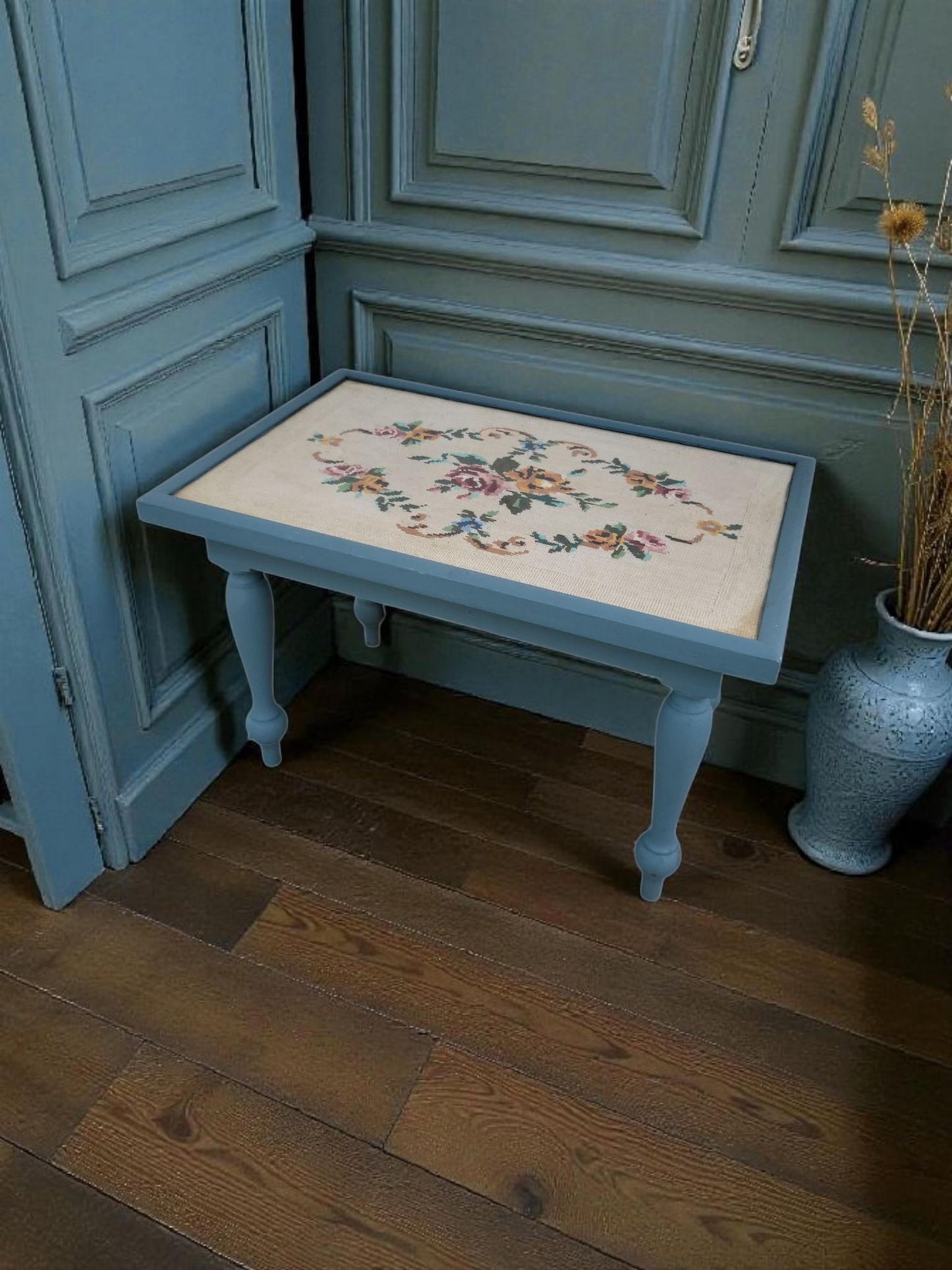 Vintage blue coffee table with hand-stitched floral tapestry under glass and turned legs