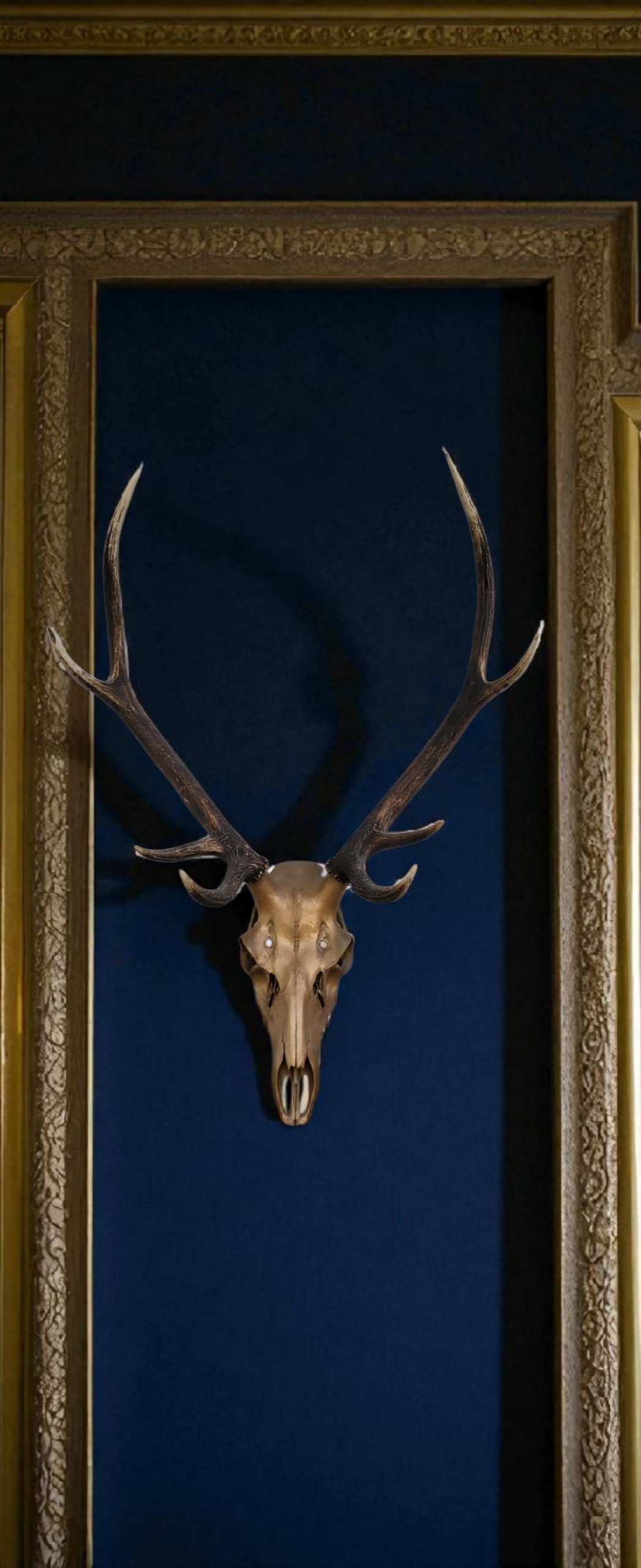 French country style gold painted deer skull with dark natural antlers leaning against a blue wall